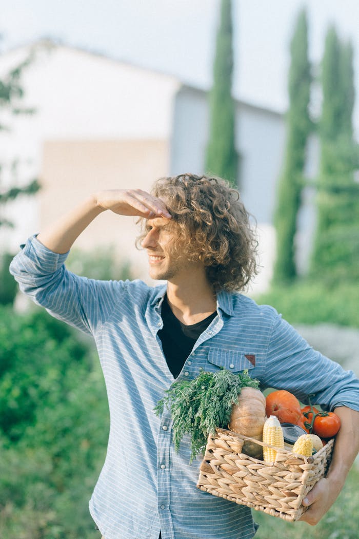 A young man holding a basket of fresh vegetables under the sun in a garden setting.